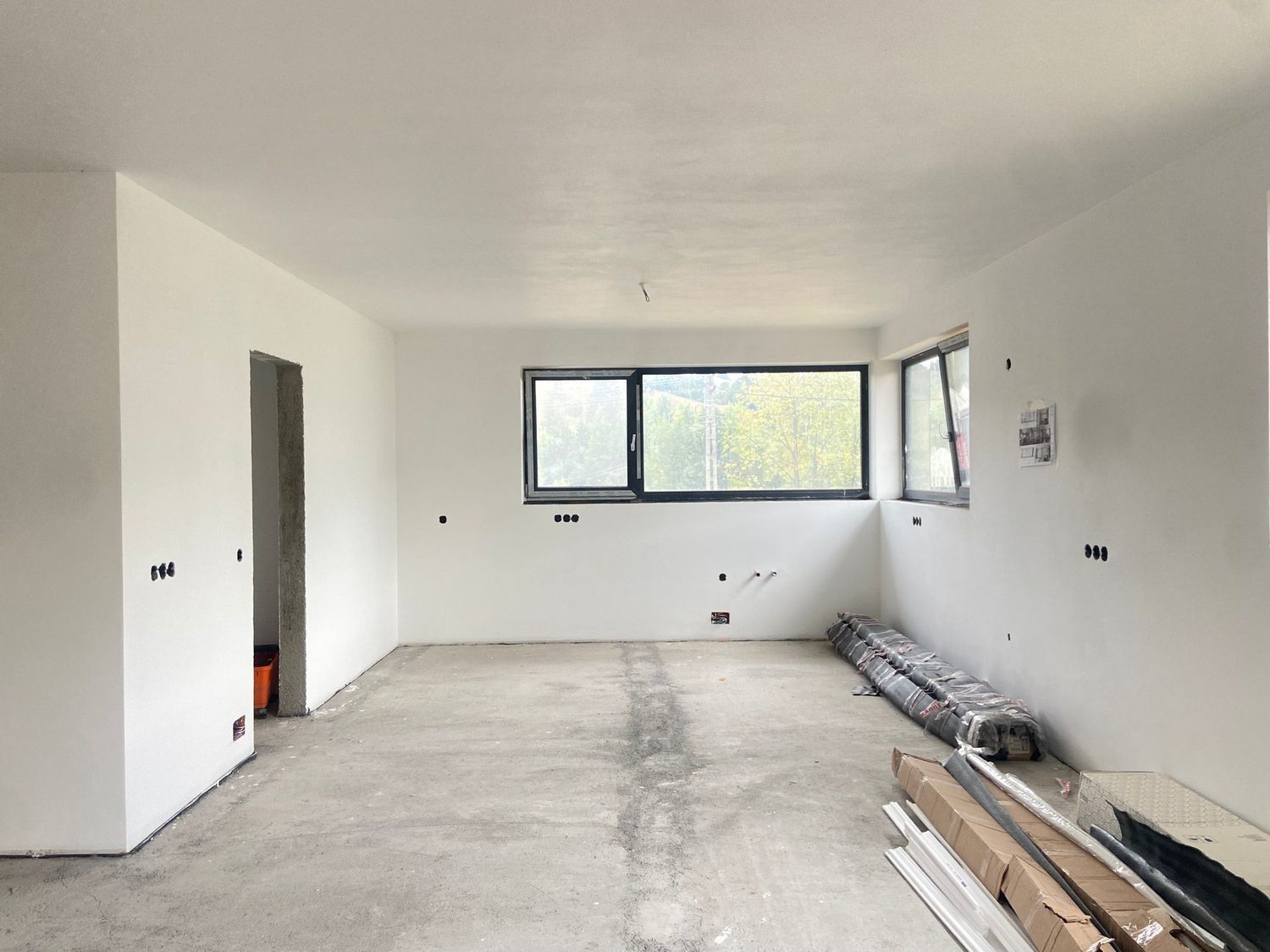 Bucătăria și zona de dining la stadiul de gri, cu tencuială albă și șapă
