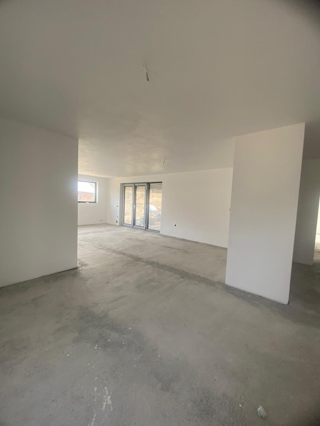 Zona de zi înainte de amenajare: spațiu gol, pereți albi și pardoseală de beton